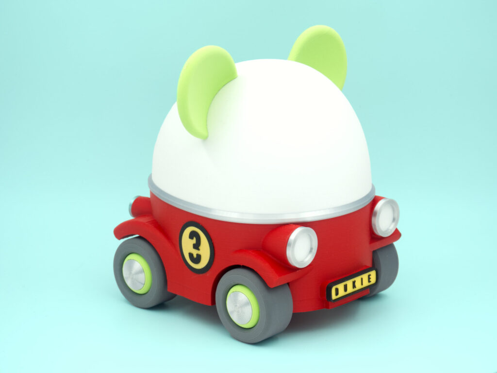 A cute My Little Cruiser toy car with animal ears in bright red and green against a blue-green gradient background. This version has a racing tag number on the sides in black and yellow.